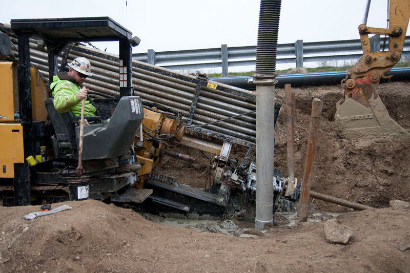 The directional boring machine pulling the new pipe back through the pilot hole it created under the river.