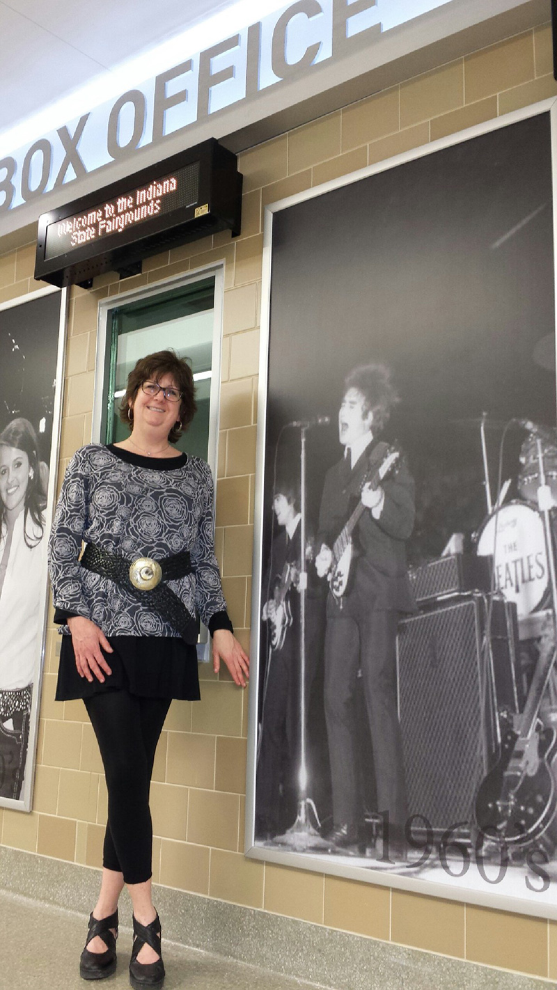Nora at the box office of the coliseum next to a Beatles poster.