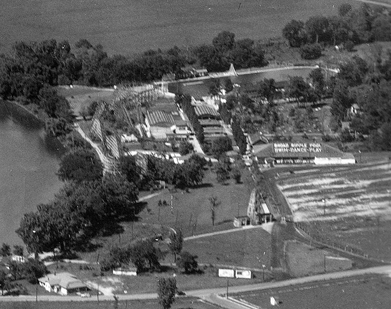 An aerial view of the amusement park at Broad Ripple Park taken in 1939. Broad Ripple Avenue is at the bottom. White River is to the left. The parking lot is in the same place today, the middle right. Visible are the roller coaster, dance hall, and famous swimming pool (where Olympic tryouts were held in 1952)